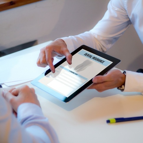 Dental team member and patient looking at dental insurance forms on tablet computer