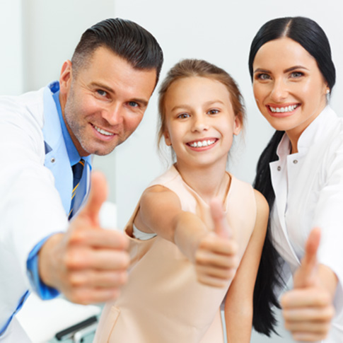 Young girl giving thumbs up alongside dental team members 