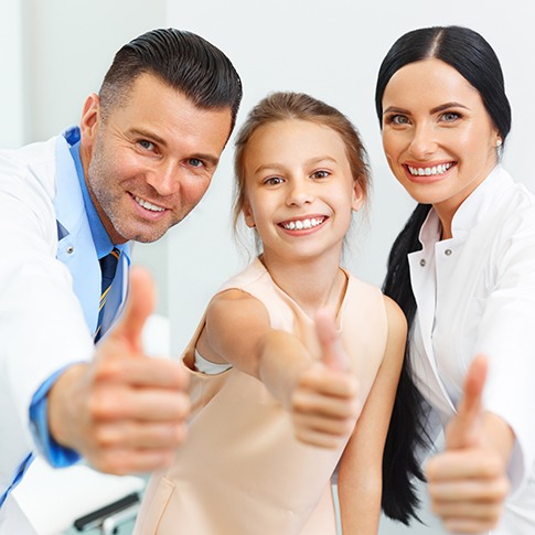 Little girl smiling and holding a thumbs up with dental team