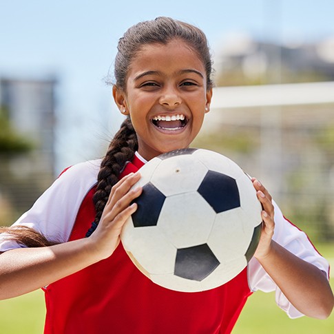 Child smiling while holding soccer ball