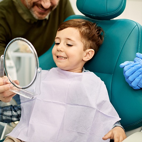 Child smiling while looking at reflection in handheld mirror