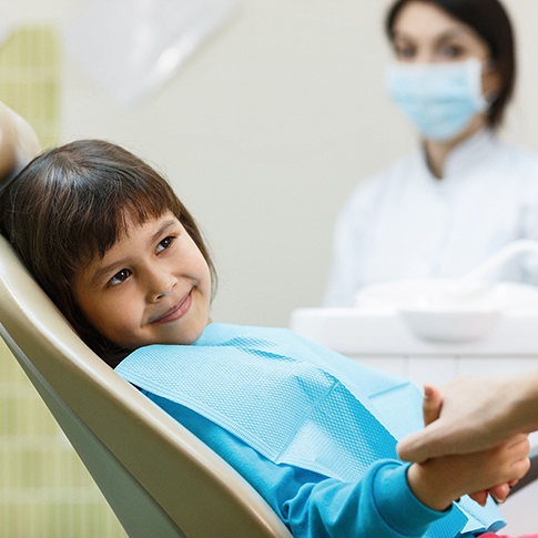 Child smiling while holding parent's hand in the treatment chair