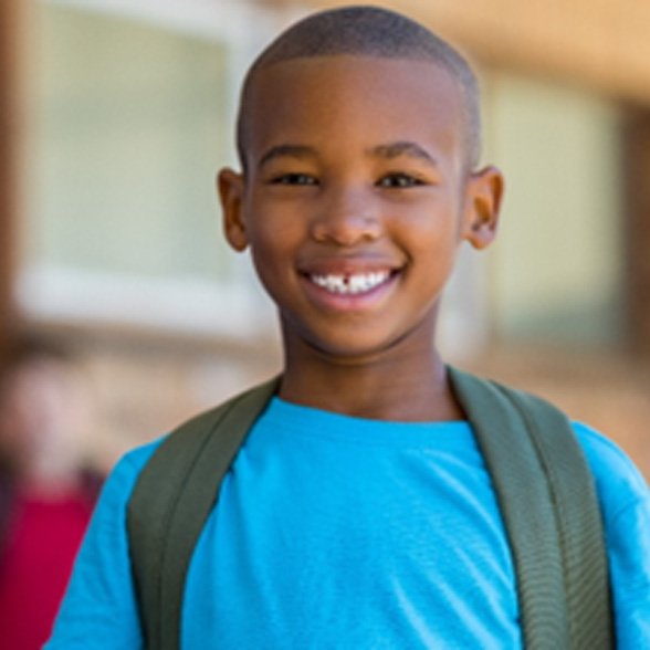Young boy in blue shirt smiling outside of his classroom