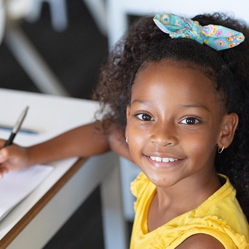 Young girl in yellow shirt smiling at school