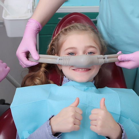 Young girl smiling while dental assistant puts nasal mask in place