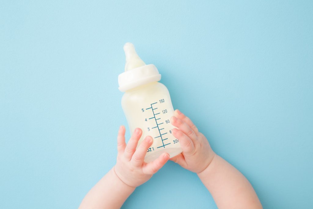 Closeup of infant holding bottle of milk