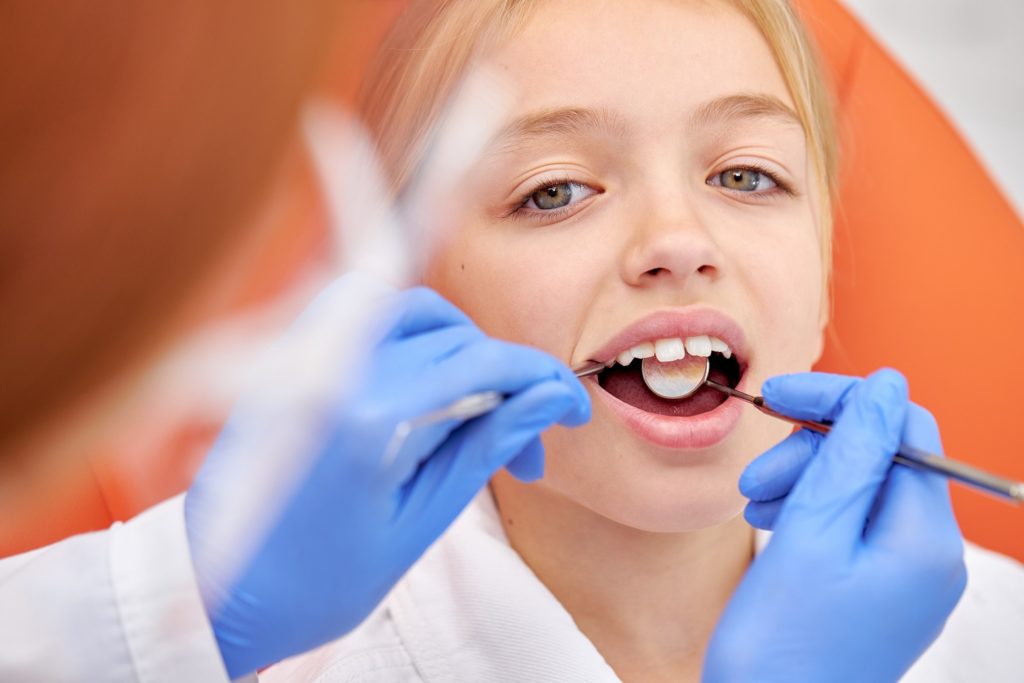 Dentist examining child's teeth with dental mirror