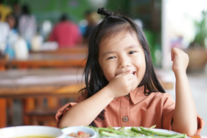 a child smiling while eating lunch at school