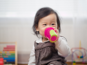 a child smiling and holding a sippy cup